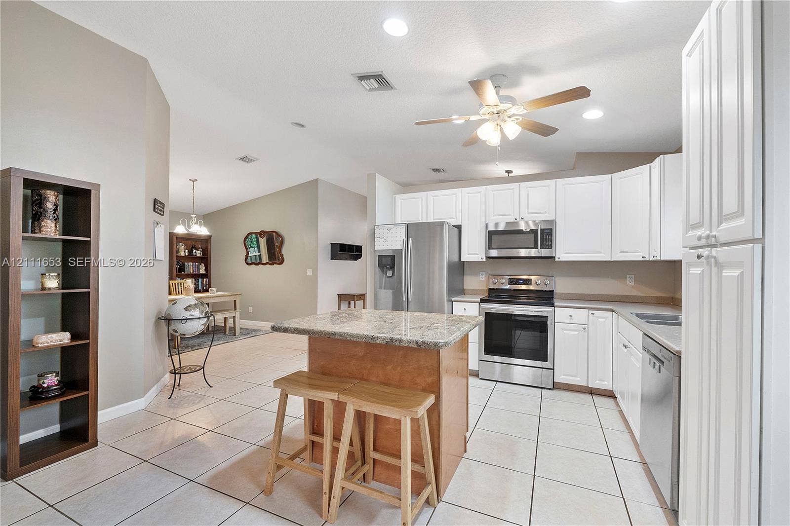 1042 NE 38th Street, Oakland Park, FL 33334 Kitchen featuring white cabinetry, stone-surface countertops, stainless steel appliances, a center island, and tile flooring