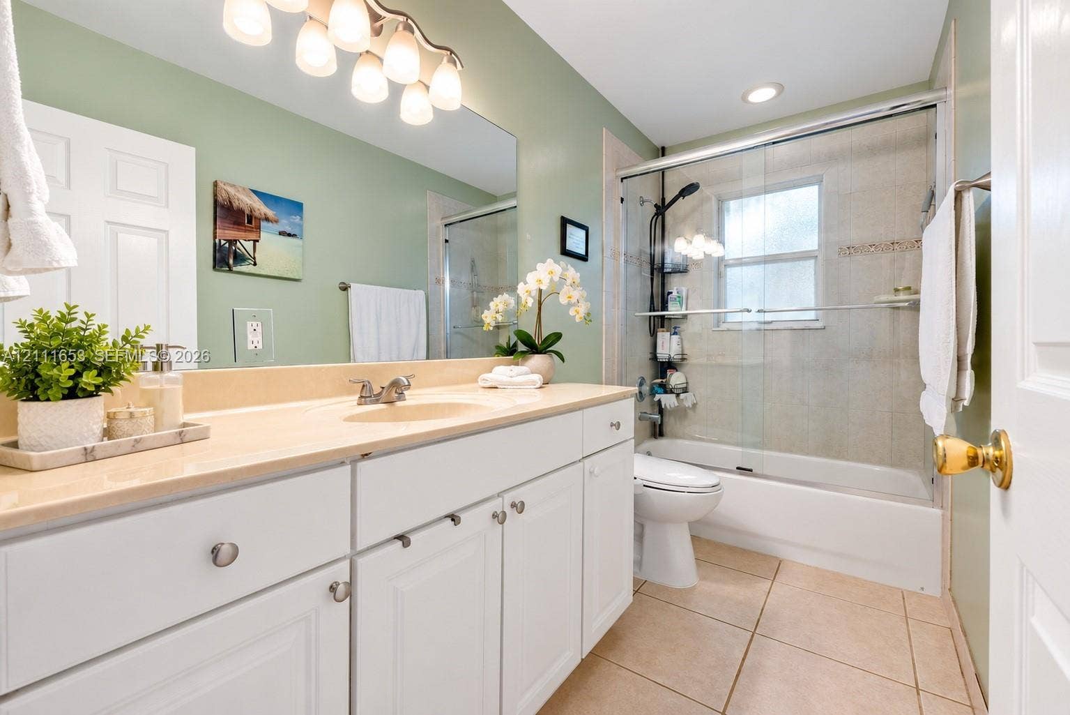 1042 NE 38th Street, Oakland Park, FL 33334 Guest Bathroom featuring white cabinetry, integrated sink, large wall-mounted mirror, ceramic tile flooring, and a shower-tub combination with glass enclosure