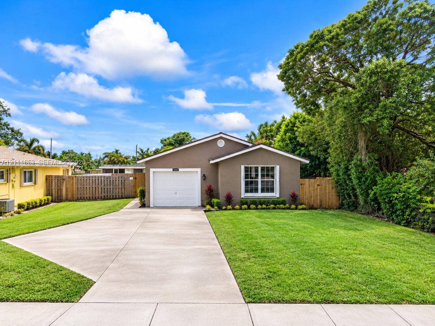 1042 NE 38th Street, Oakland Park, FL 33334 Single-story residence featuring a concrete driveway, attached garage, and wood privacy fencing
