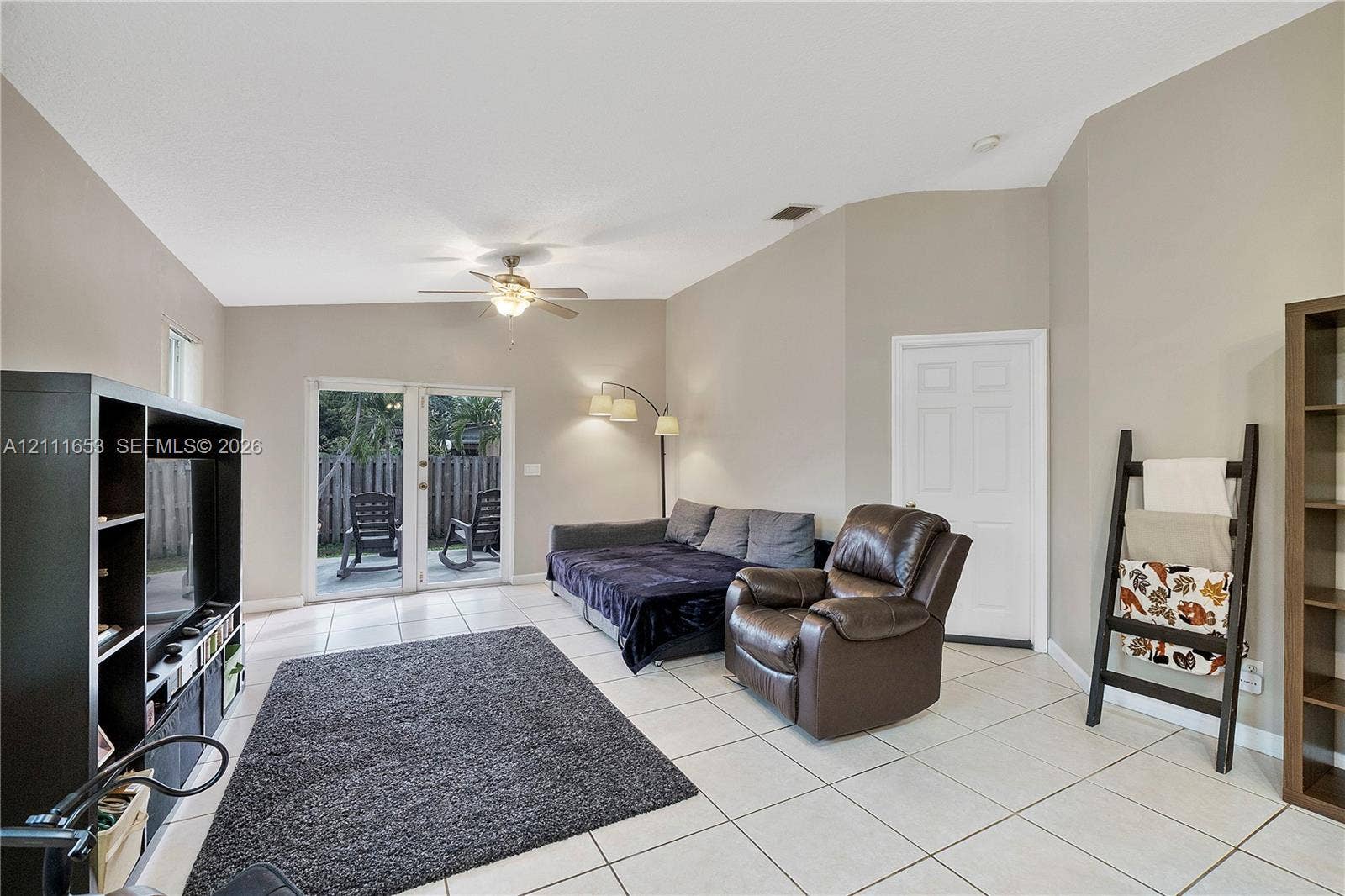 1042 NE 38th Street, Oakland Park, FL 33334 Living area featuring vaulted ceilings, neutral wall tones, large-format tile flooring, a center-mounted ceiling fan, and double-glass doors providing patio access
