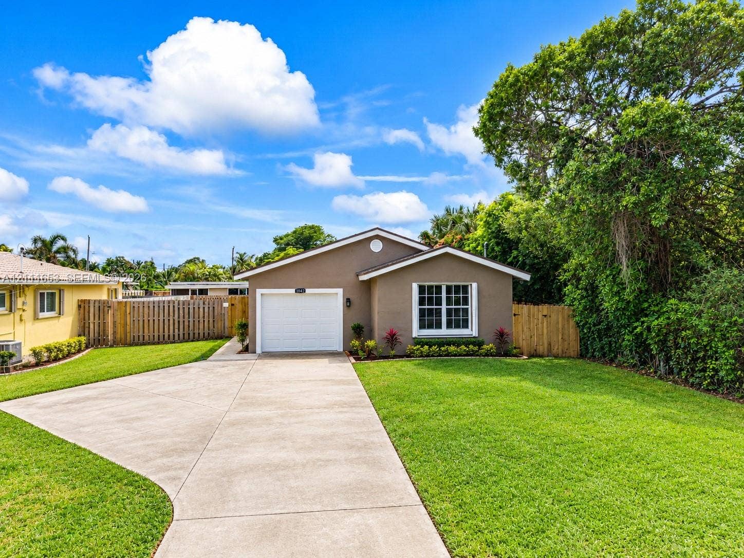 1042 NE 38th Street, Oakland Park, FL 33334 Single-story residence featuring a concrete driveway, attached one-car garage, and wooden privacy fencing