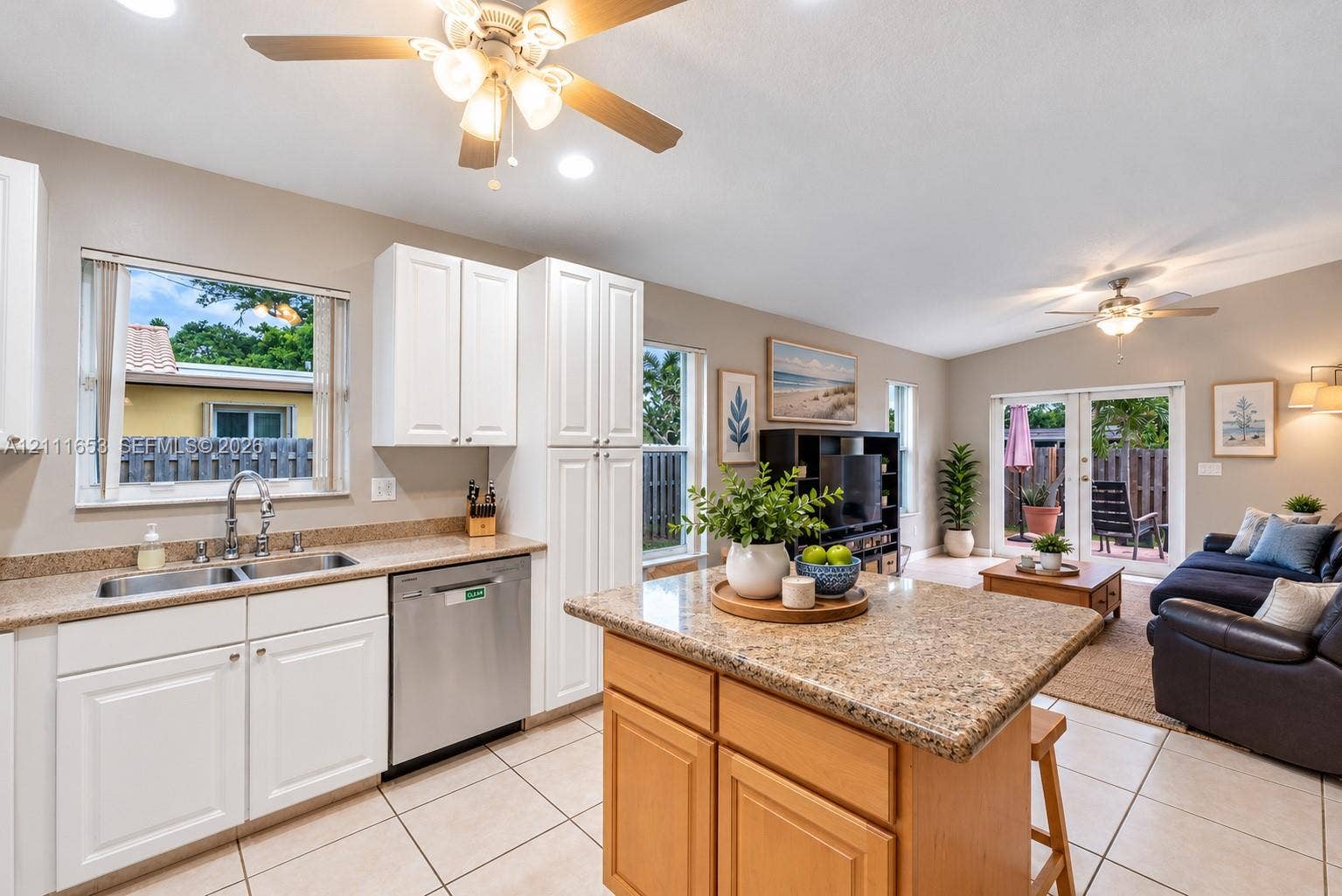 1042 NE 38th Street, Oakland Park, FL 33334 Kitchen featuring white cabinetry, stone-finish countertops, stainless steel dual-basin sink, center island, and neutral tile flooring