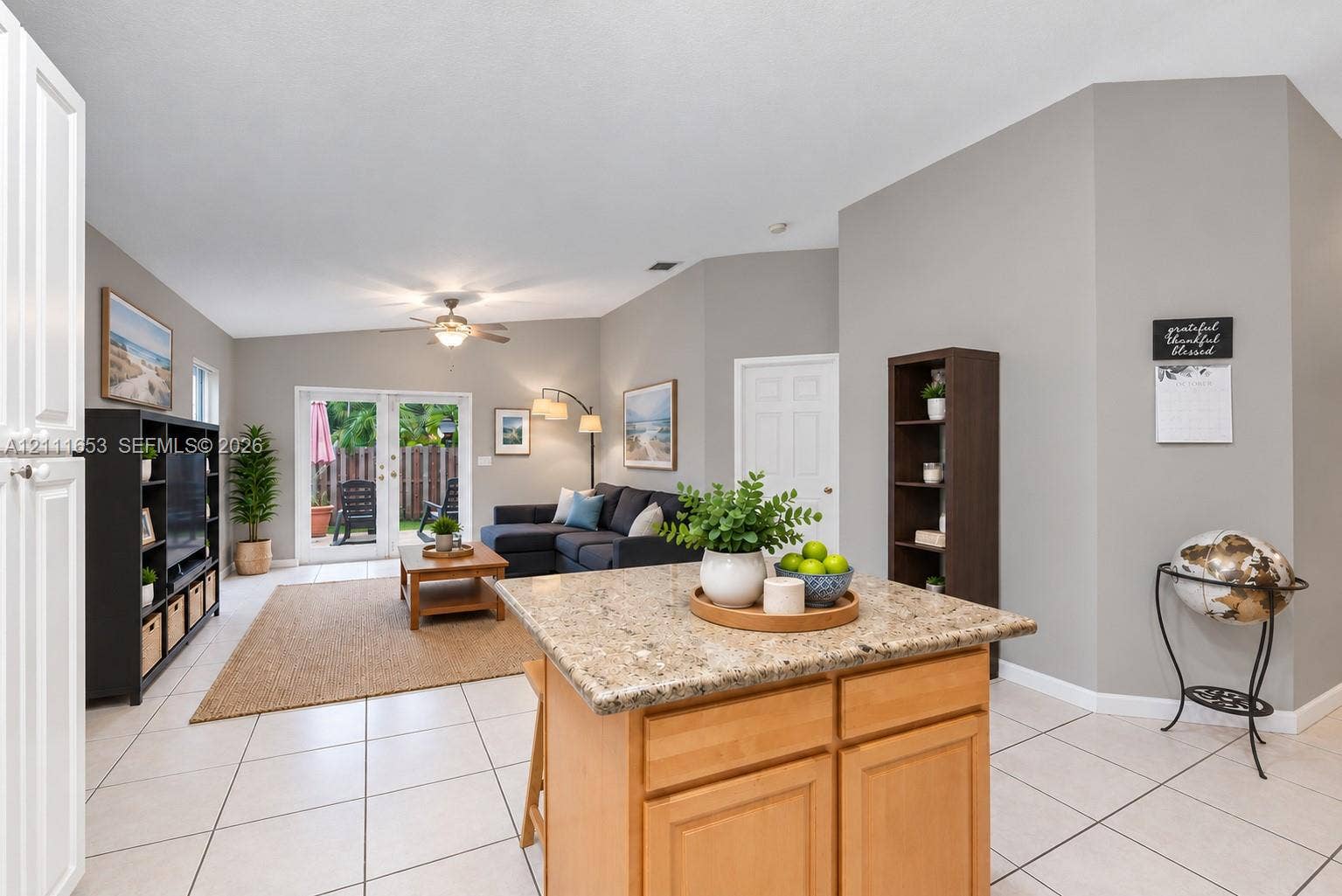 1042 NE 38th Street, Oakland Park, FL 33334 Kitchen island featuring a stone-composite countertop and natural-finish cabinetry, complemented by light-toned floor tile and French doors with integrated glass panels