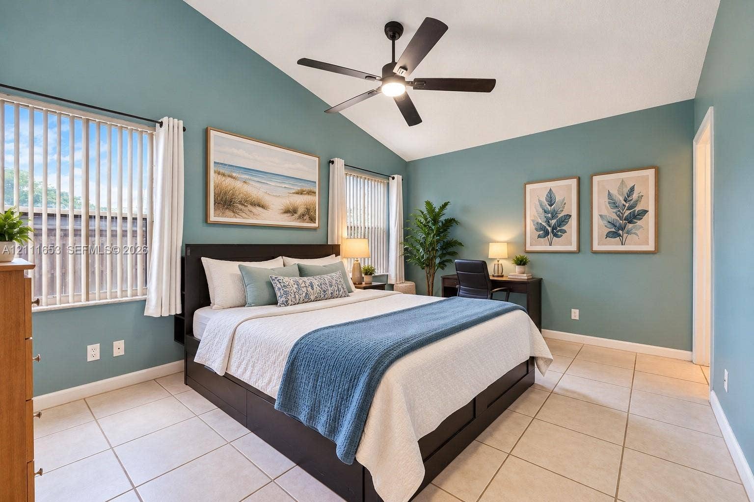 1042 NE 38th Street, Oakland Park, FL 33334 Primary Bedroom vaulted ceilings featuring a central matte black ceiling fan with an integrated light fixture, light-toned ceramic tile flooring, and multiple windows with vertical blinds