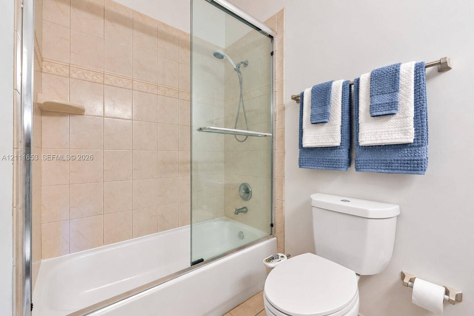 1042 NE 38th Street, Oakland Park, FL 33334 Primary Bath tub and shower combination featuring a glass sliding door, ceramic wall tile surround, and metal hardware