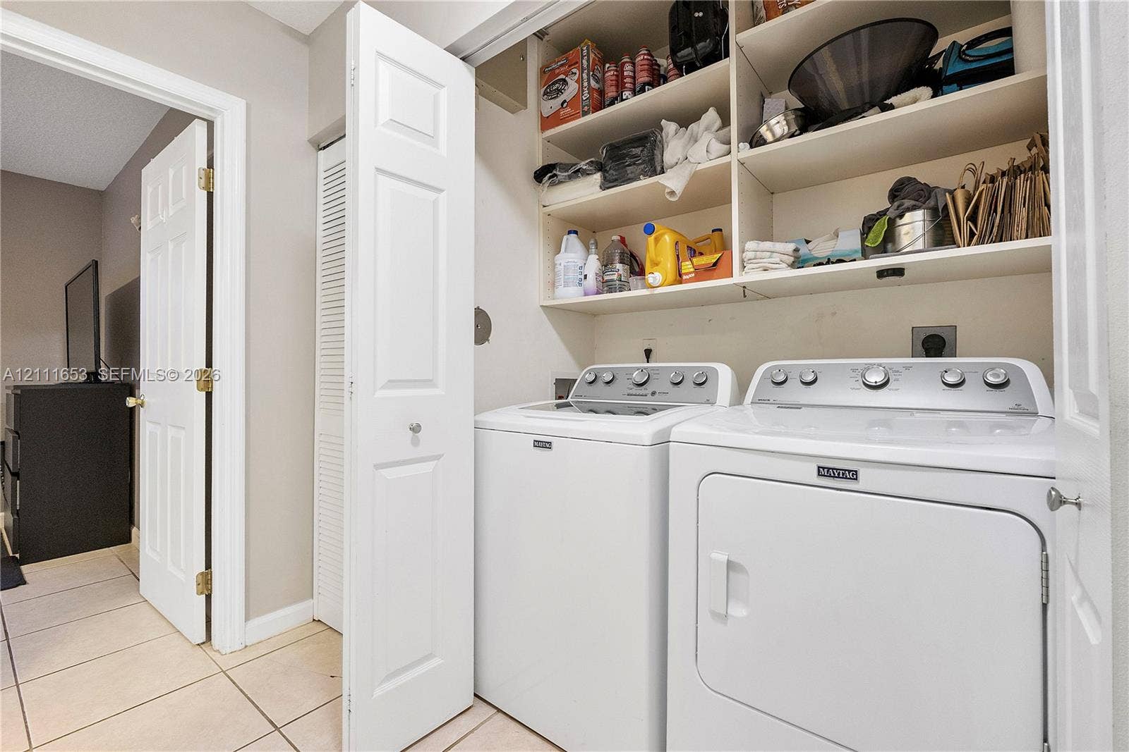 1042 NE 38th Street, Oakland Park, FL 33334 Laundry area featuring ceramic tile flooring, built-in overhead storage shelving, and bi-fold closet doors