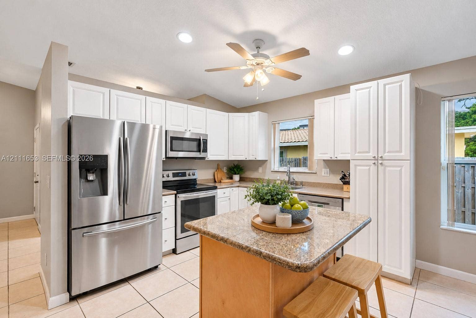 1042 NE 38th Street, Oakland Park, FL 33334 Kitchen featuring white cabinetry, stone-finish countertops, stainless steel appliances, a center island, and ceramic tile flooring