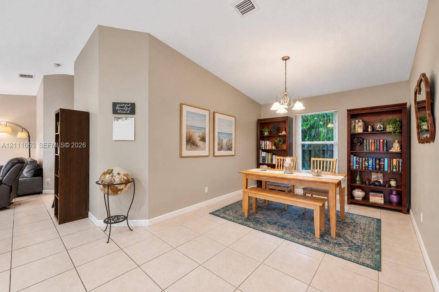 1042 NE 38th Street, Oakland Park, FL 33334 Neutral-toned interior featuring ceramic tile flooring, vaulted ceilings, and a decorative multi-arm chandelier