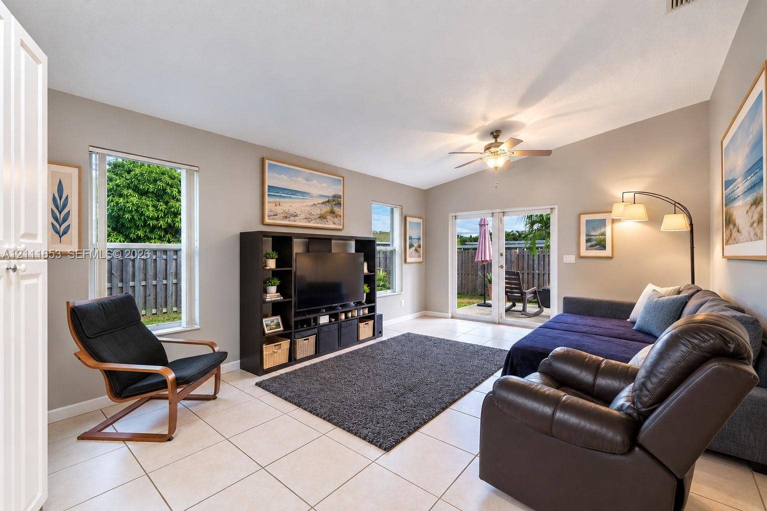 1042 NE 38th Street, Oakland Park, FL 33334 Neutral-toned interior featuring large-format tile flooring, vaulted ceilings, a central ceiling fan with integrated lighting, and glass double doors providing exterior access