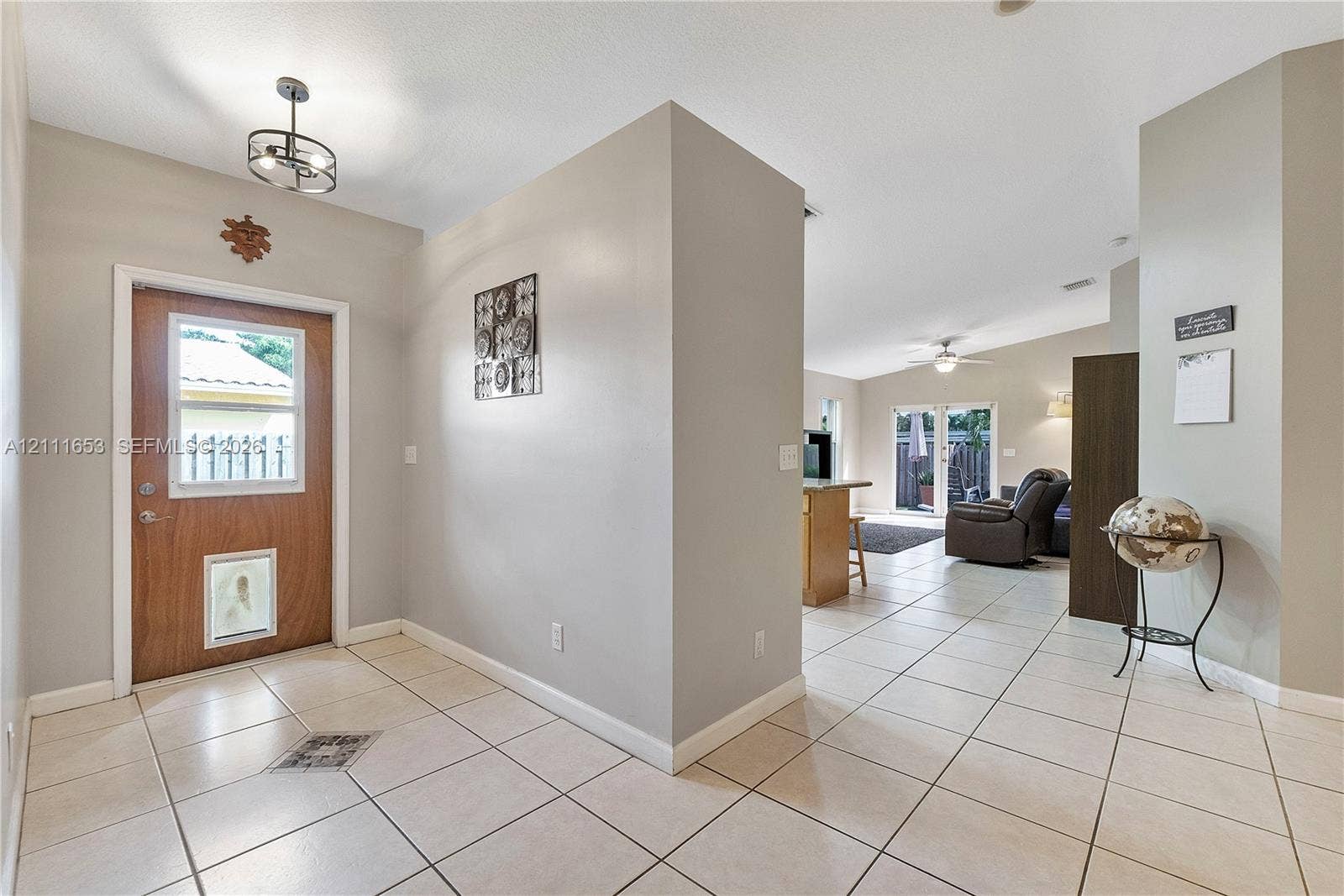 1042 NE 38th Street, Oakland Park, FL 33334 Entryway featuring tile flooring, neutral wall paint, and a wood-finish exterior door with a glass inset