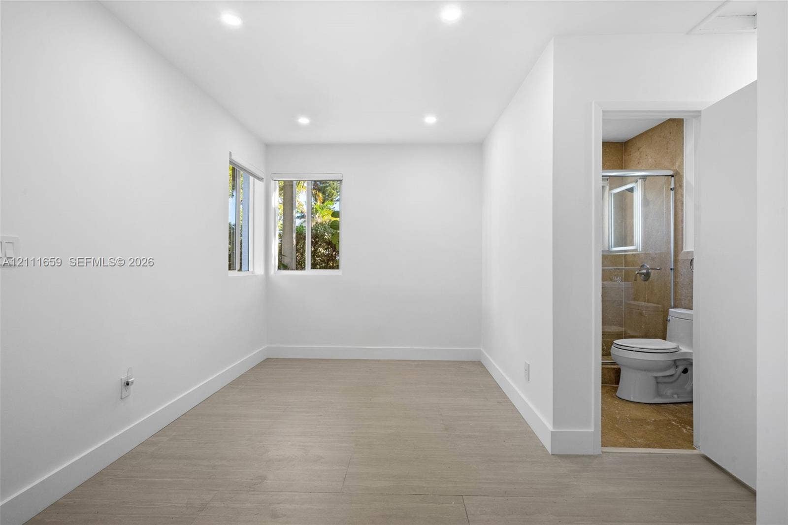 338 Taylor Street, #2, Hollywood, Hollywood, FL 33019 Interior space featuring wood-finish flooring, recessed lighting, and dual windows, with an attached bathroom showcasing tile wall surfacing, a glass-enclosed shower, and a vitreous china toilet