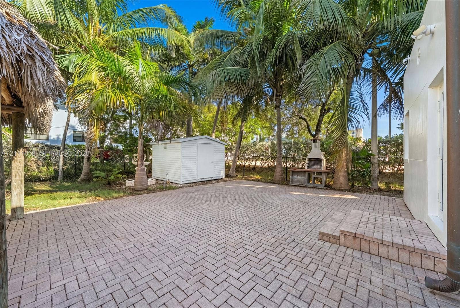 338 Taylor Street, #2, Hollywood, Hollywood, FL 33019 Outdoor space featuring a herringbone-patterned paver patio, permanent masonry outdoor fireplace, detached storage structure, and mature palm trees
