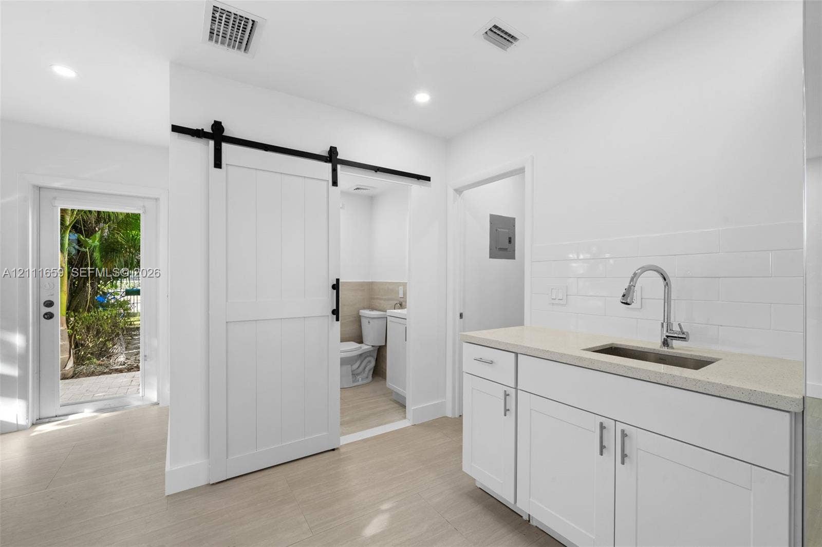 338 Taylor Street, #2, Hollywood, Hollywood, FL 33019 White shaker-style cabinetry with neutral solid-surface countertop, subway tile backsplash, stainless steel under-mount sink, and sliding barn-style door