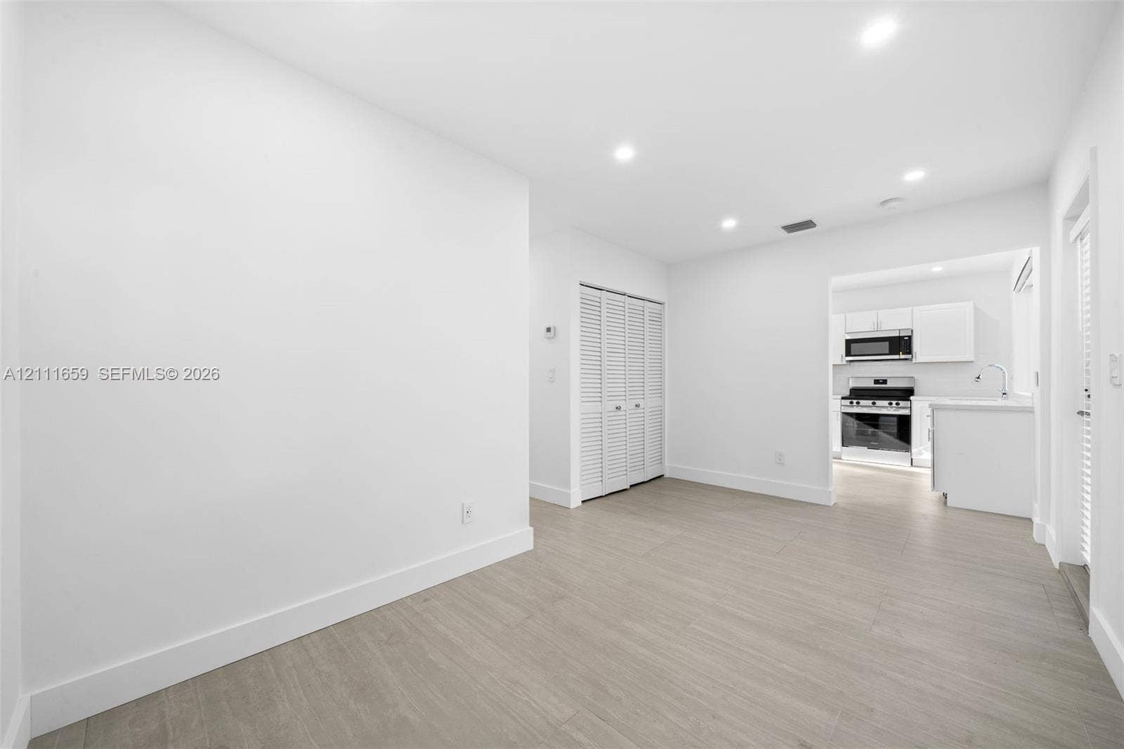 338 Taylor Street, #2, Hollywood, Hollywood, FL 33019 Neutral-toned interior space featuring wood-finish flooring, recessed lighting, white louvered closet doors, and a kitchen equipped with stainless steel appliances