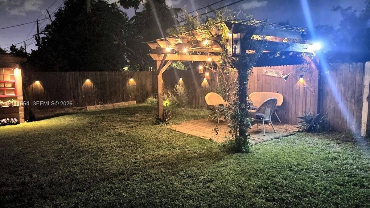 Backyard featuring a wood pergola, custom wood-fencing with wall-mounted lighting, and a manicured lawn