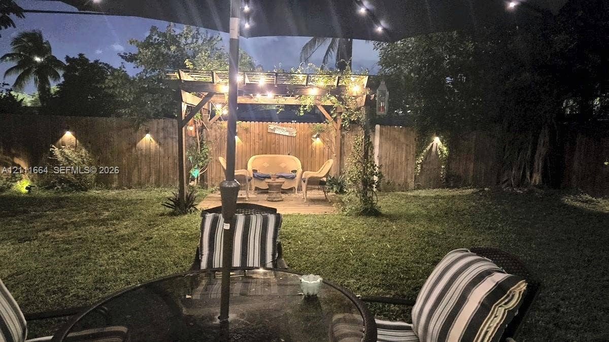 Private backyard featuring a wooden pergola, perimeter wood fencing, and mounted wall lighting