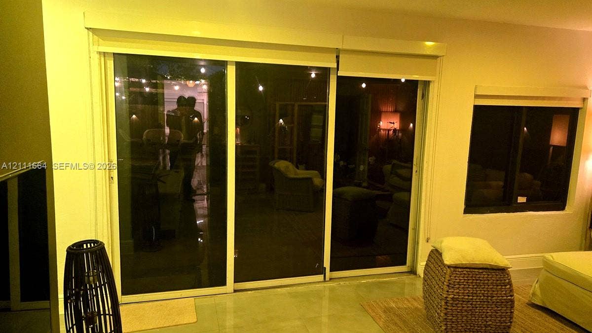 Large sliding glass doors with roller shades and a square-pane window featuring dark frames and smooth-finish interior walls