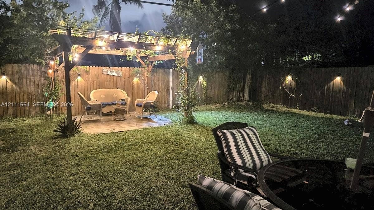 Backyard featuring a wooden pergola, privacy fencing, integrated wall-mounted lighting, and a stone-paver patio