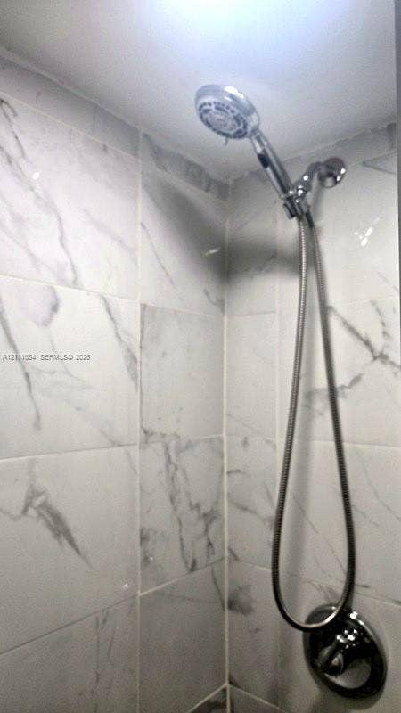 Shower enclosure featuring polished chrome handheld showerhead with adjustable hose and large-format white wall tile with grey veining