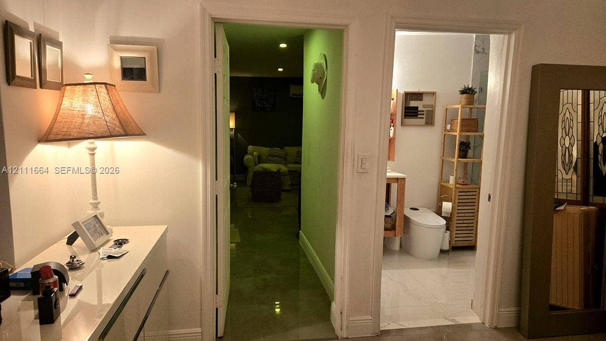 Glossy finish floor tiles and white wall finishes throughout with a wall-mounted vanity featuring a vessel sink and a minimalist elongated toilet