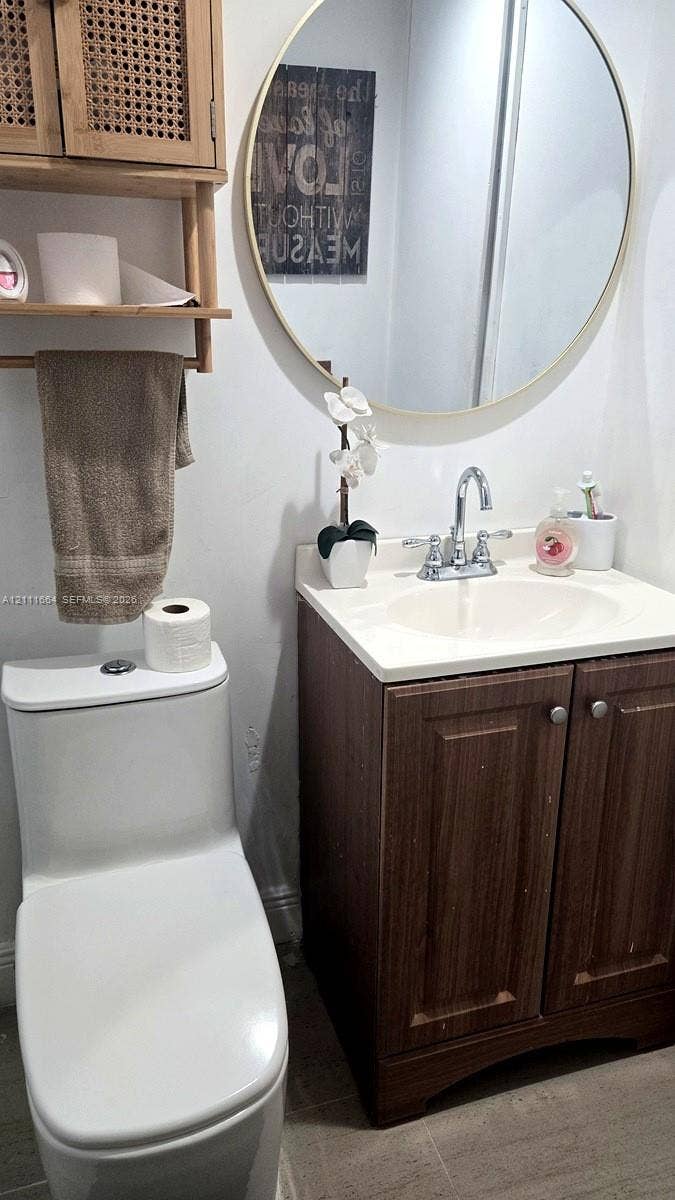 Vanity featuring wood-finish cabinetry, light-toned countertop with an integrated basin, circular mirror with a metallic frame, and wall-mounted cane-accented shelving