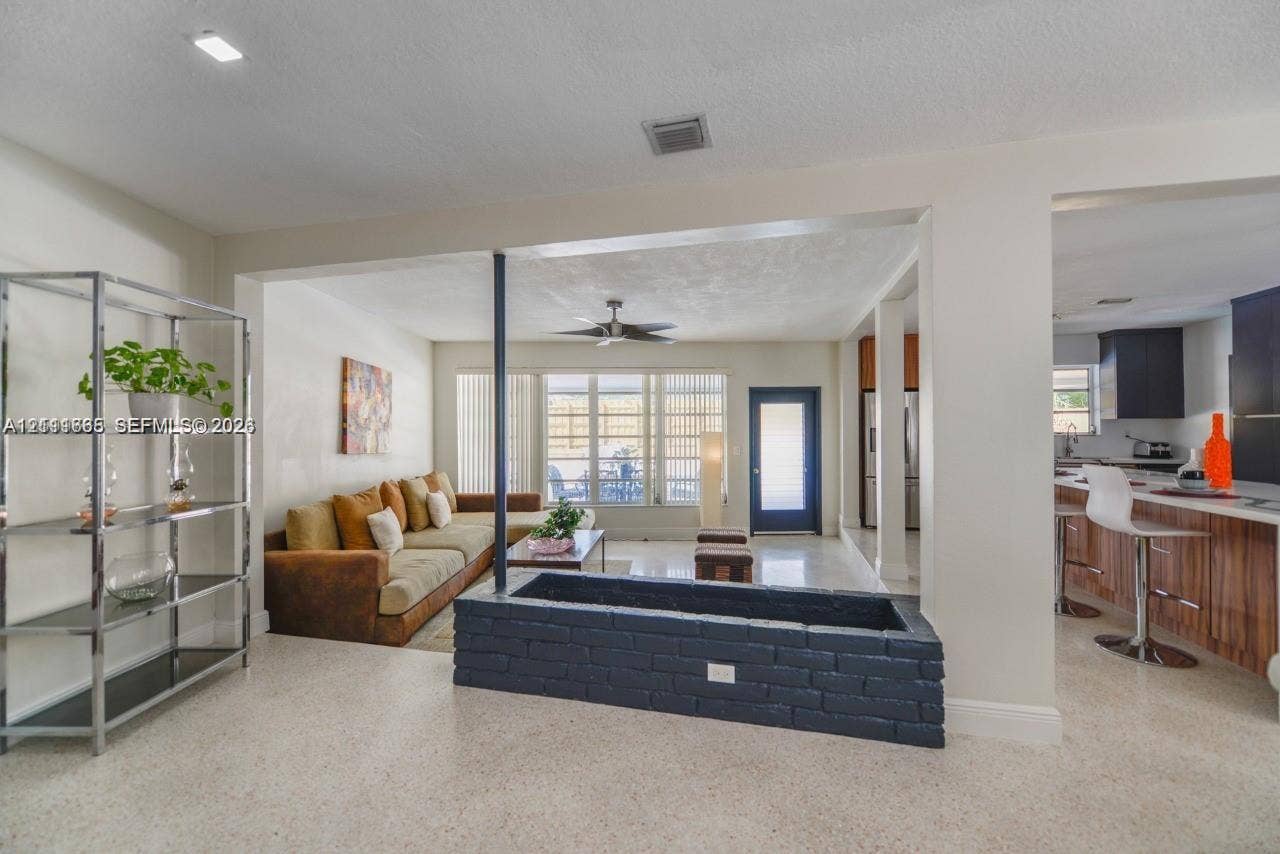 Open-concept interior featuring light-toned stone-finish flooring, recessed lighting, and a painted brick built-in planter with a central support pillar