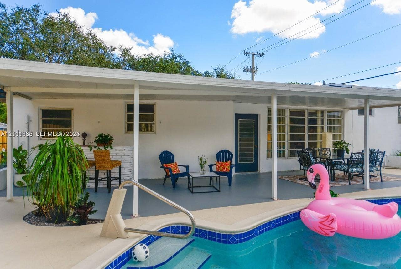 Covered patio featuring a painted concrete floor, a built-in exterior bar, and a rectangular swimming pool with tiled coping and metal handrails