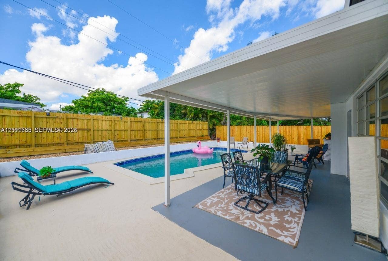 Covered outdoor patio featuring a concrete deck and a rectangular swimming pool enclosed by wooden privacy fencing