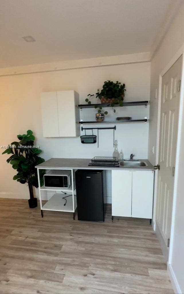 Kitchenette featuring white cabinetry, wood-finish flooring, a stainless steel sink with a metallic faucet, and open metal shelving