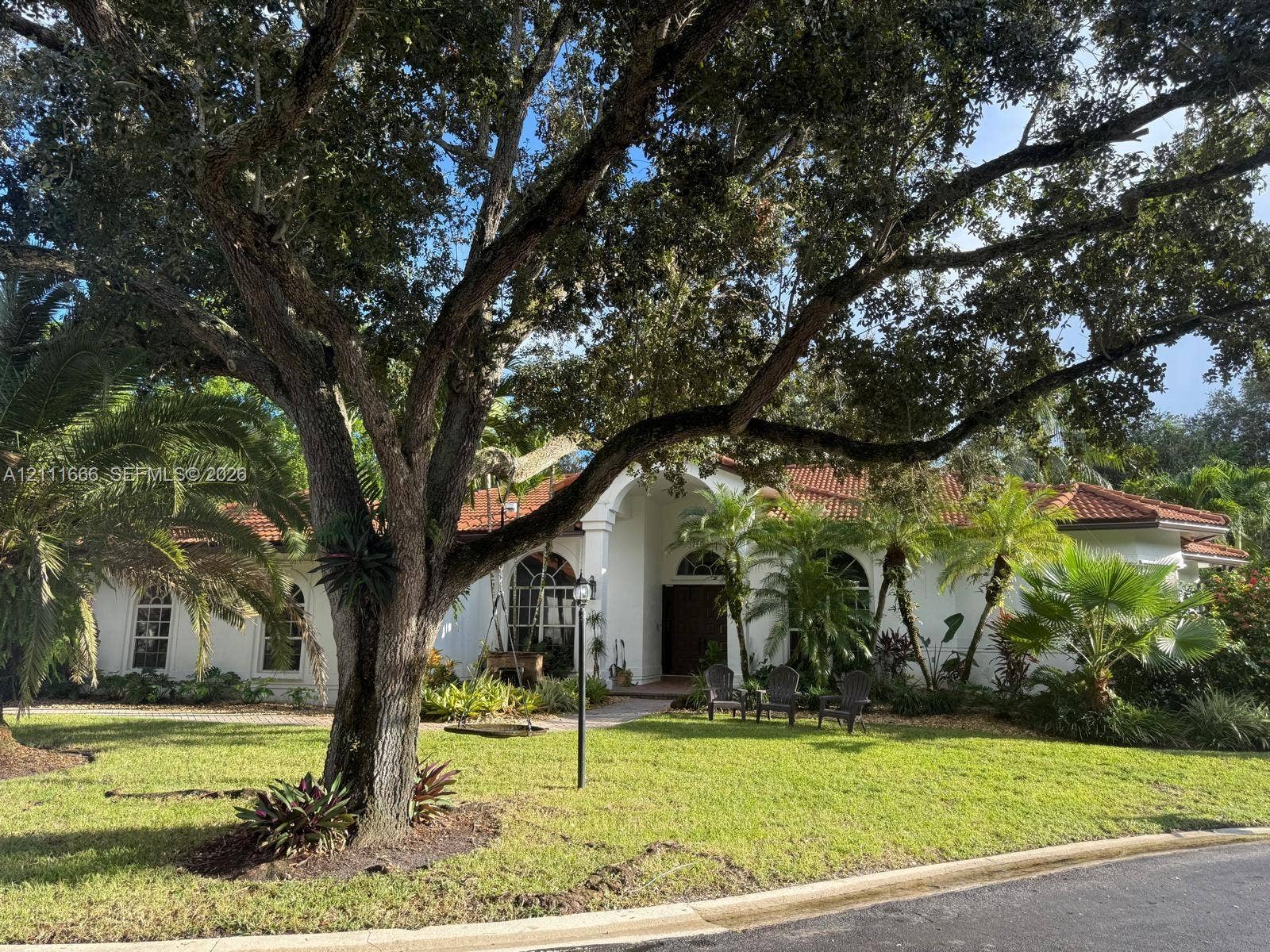 6520 NW 95th Lane, Parkland, FL 33076 Stucco exterior featuring arched windows, a covered entryway with an arched opening, a clay tile roof, and mature landscaping