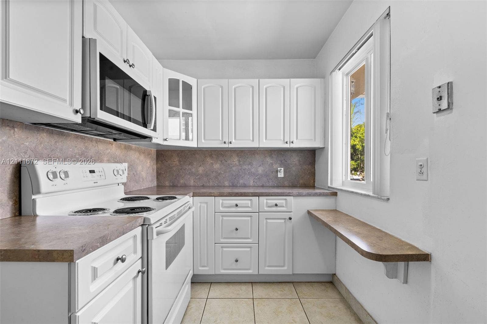 Kitchen featuring white cabinetry, solid-surface countertops, tile flooring, a built-in microwave, and a wall-mounted breakfast bar