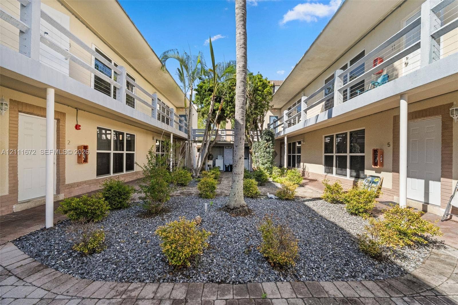 Central courtyard featuring gravel landscaping, mature palm trees, multi-level railed walkways, and paver-edged pathways