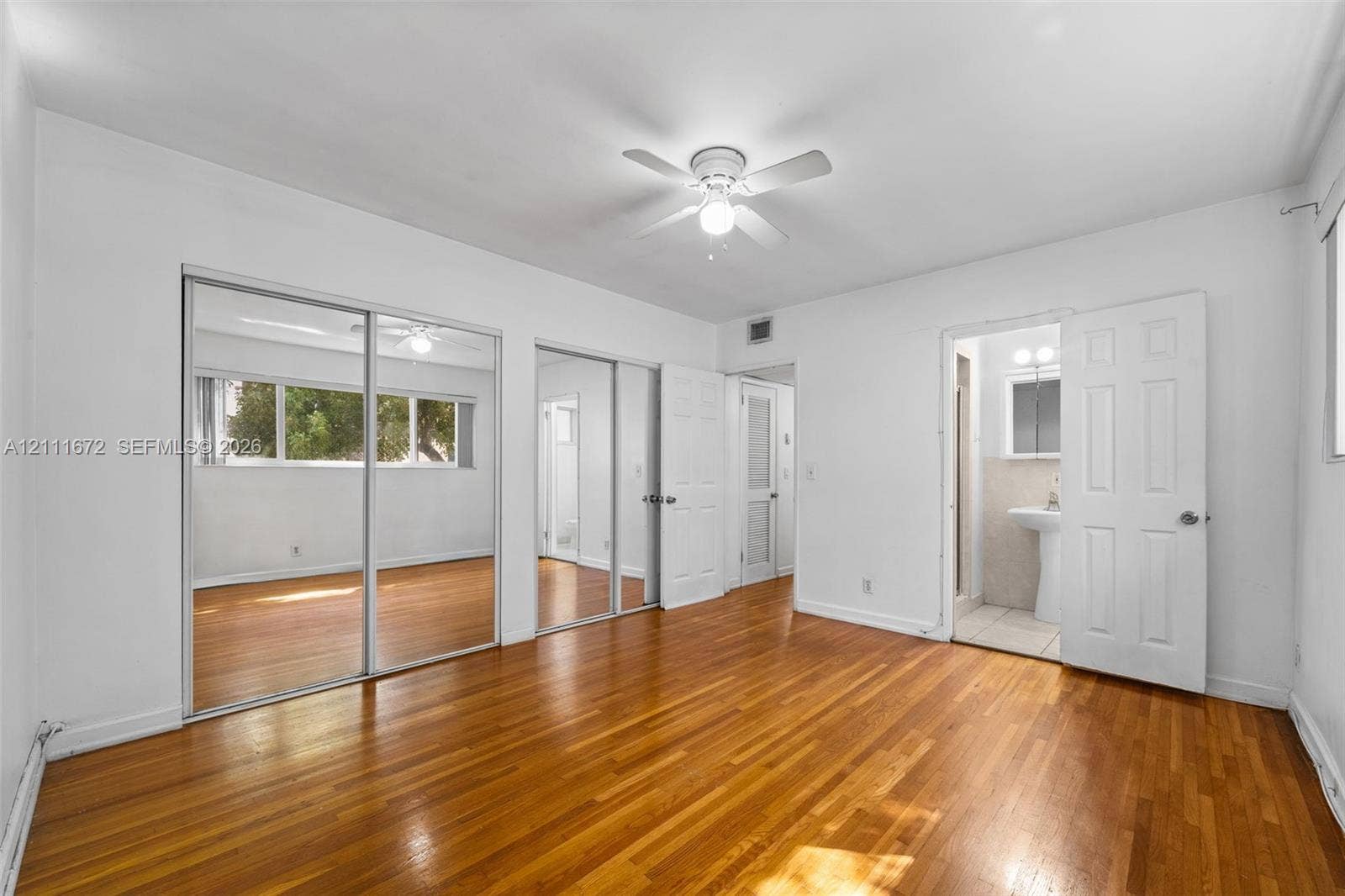 Wood-finish flooring, dual sliding mirrored closet doors, white panel doors, and a ceiling-mounted light fixture