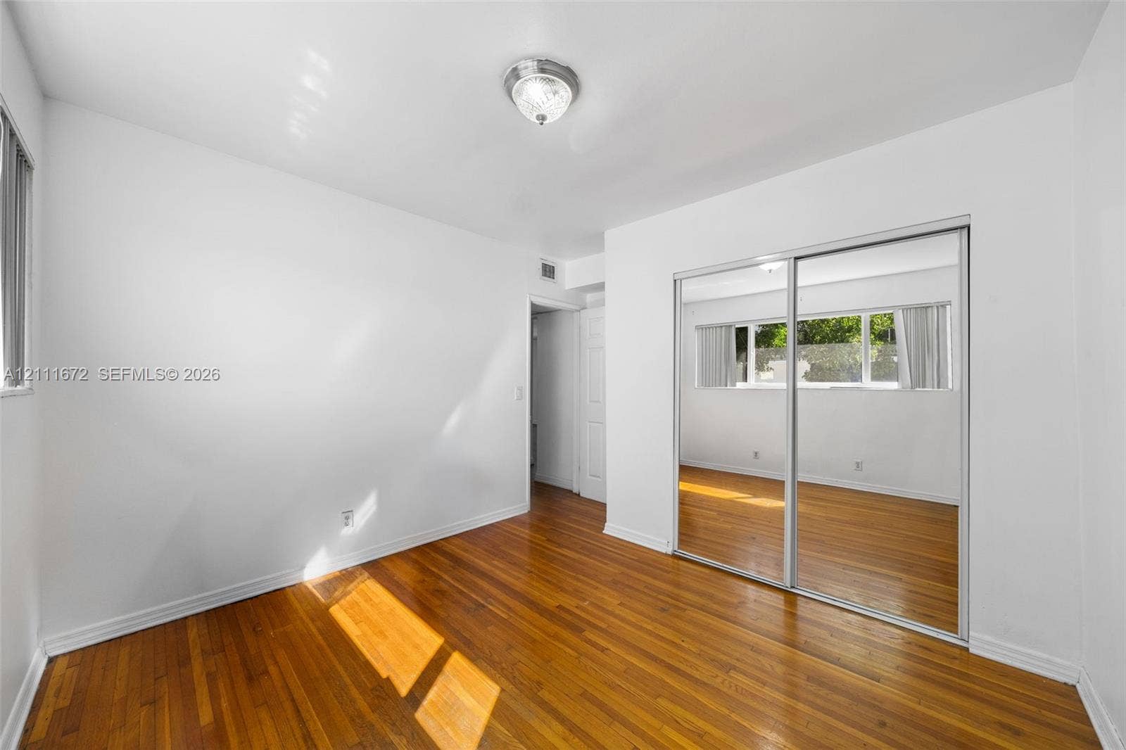 Interior room featuring wood-finish flooring, sliding mirrored closet doors, a single-light flush mount ceiling fixture, and dual-pane windows