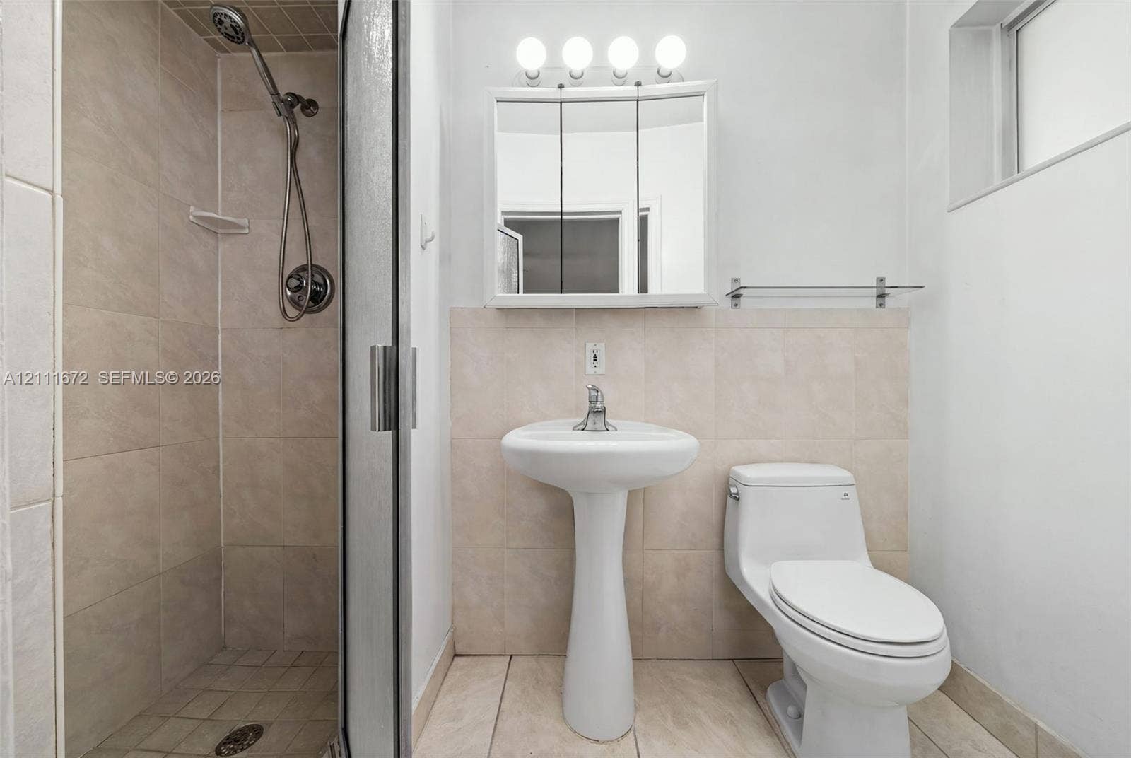 Bathroom featuring a tiled stall shower with a handheld fixture, pedestal sink, mirrored medicine cabinet with integrated lighting, and tile flooring