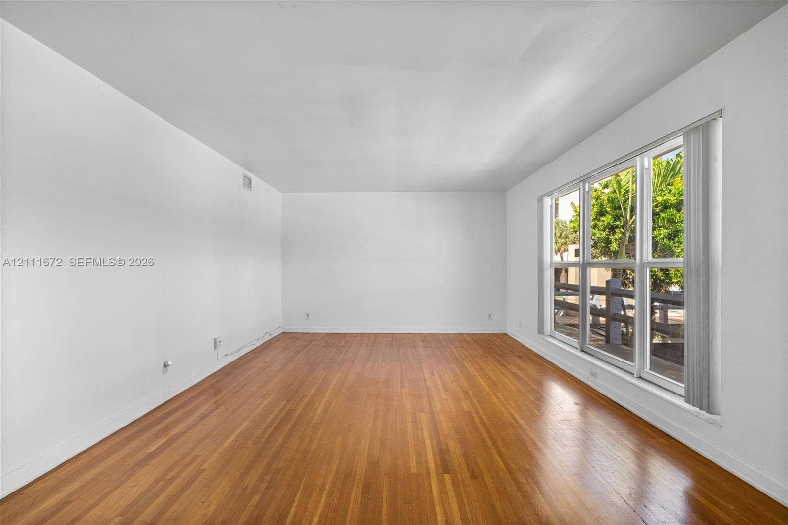 Interior space featuring wood-finish flooring, white walls, and a large multi-pane window with vertical blinds