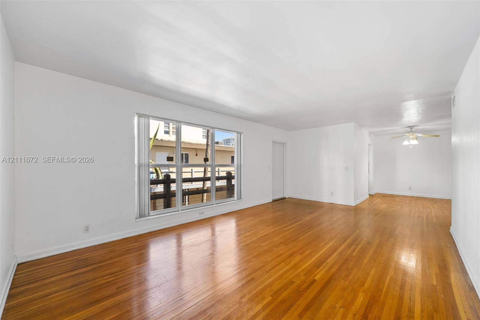 Living area featuring wood-finish flooring, large multi-pane windows, and a ceiling fan with integrated lighting