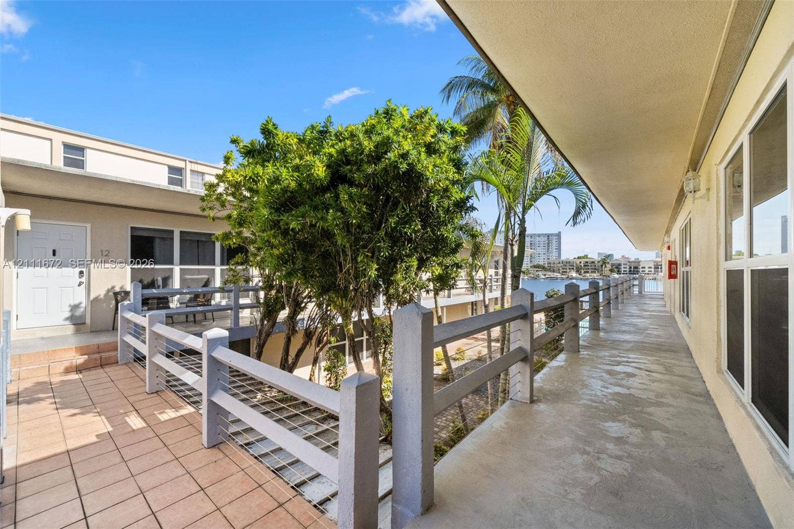 Covered exterior walkway featuring tile flooring, metal railings, and natural landscaping