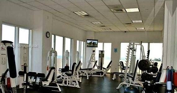 Fitness center featuring floor-to-ceiling windows, drop ceiling with recessed lighting, and rubberized flooring