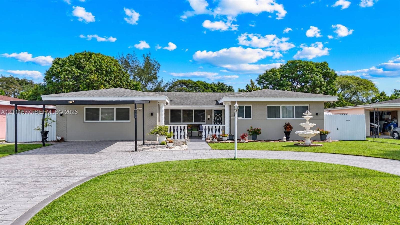 1921 Acapulco Drive, Miramar, FL 33023 Single-story exterior featuring a circular paver driveway, covered carport, decorative fountain, and white balustrade porch railing
