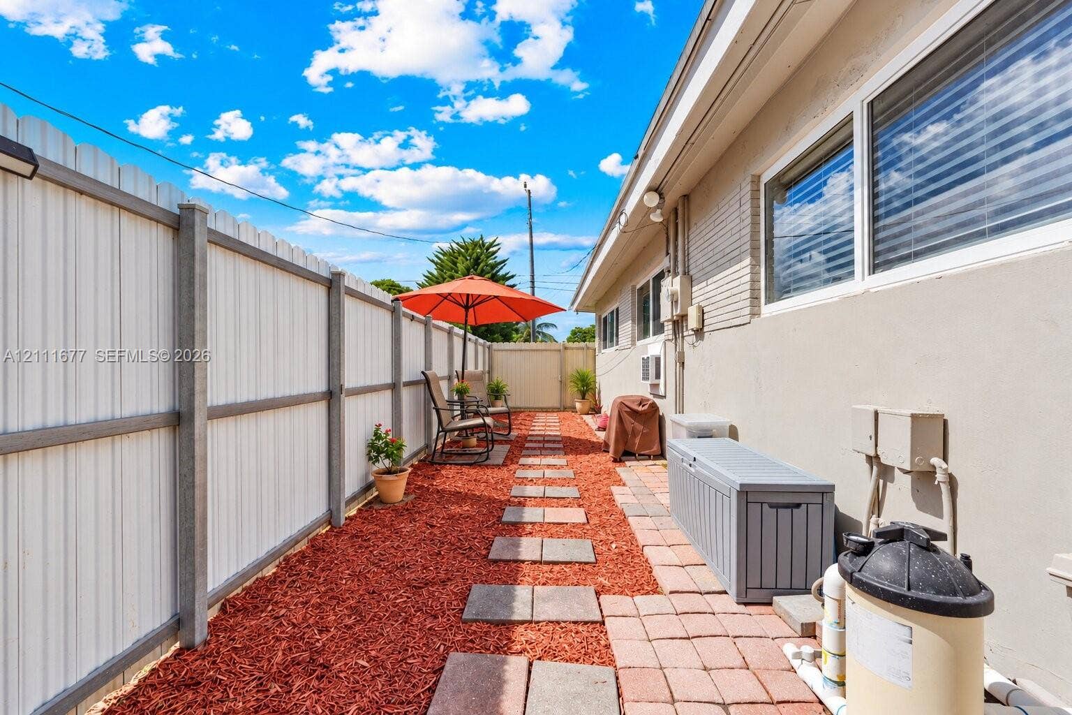 1921 Acapulco Drive, Miramar, FL 33023 Side yard featuring a perimeter metal privacy fence, red mulch ground cover, and square concrete paver pathway