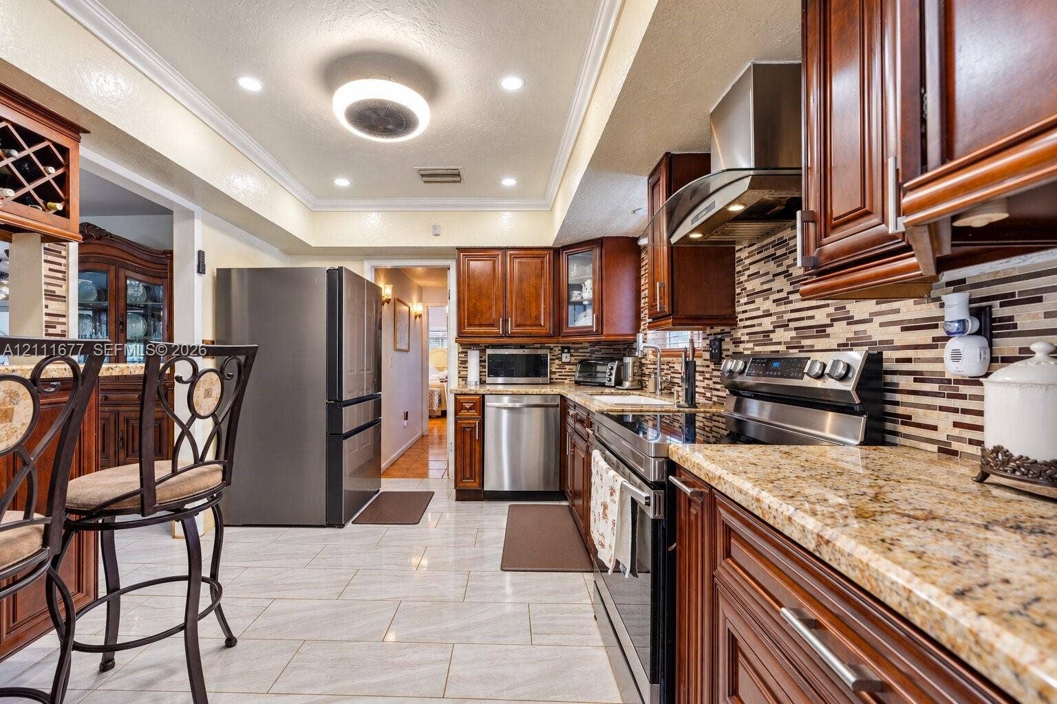 1921 Acapulco Drive, Miramar, FL 33023 Kitchen featuring wood cabinetry, stone countertops, stainless steel appliances, multi-tonal backsplash, and tile flooring