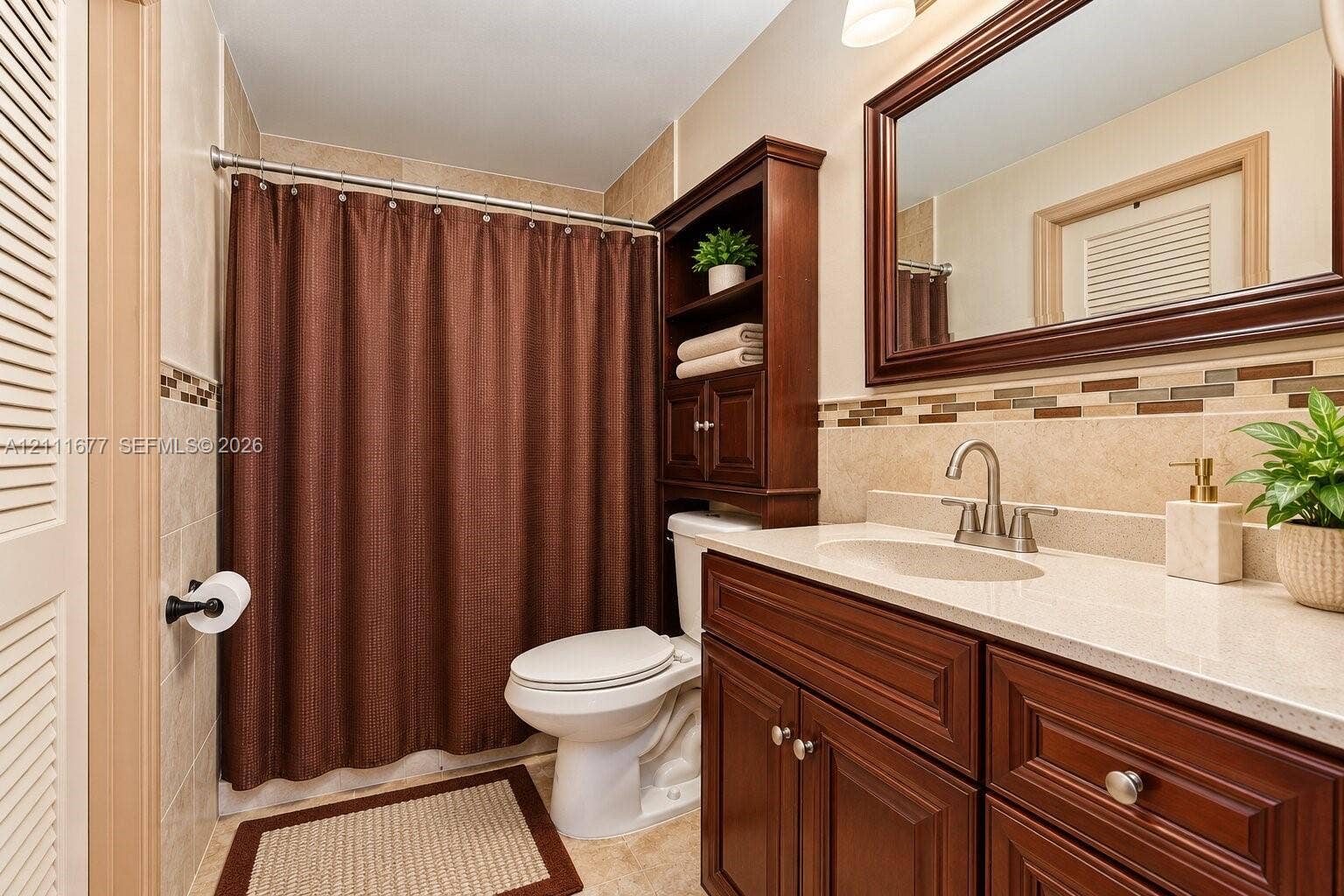 1921 Acapulco Drive, Miramar, FL 33023 Bathroom featuring a vanity with wood-finish cabinetry, light-toned countertop, integrated shelving, framed wall mirror, and decorative tile backsplash