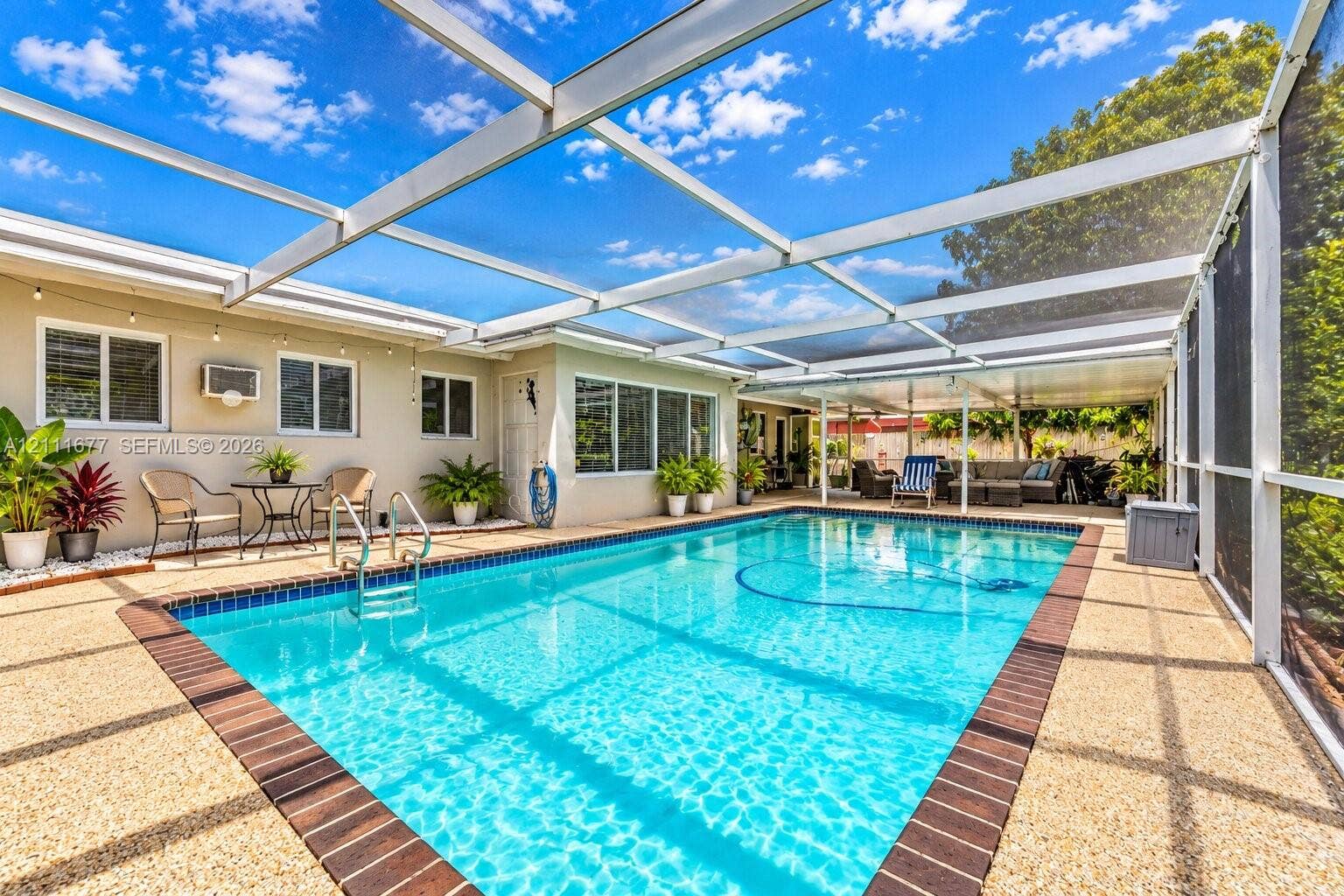 1921 Acapulco Drive, Miramar, FL 33023 Screened lanai featuring a swimming pool with dark-toned tile coping, a pebbled pool deck, and a metal-framed enclosure