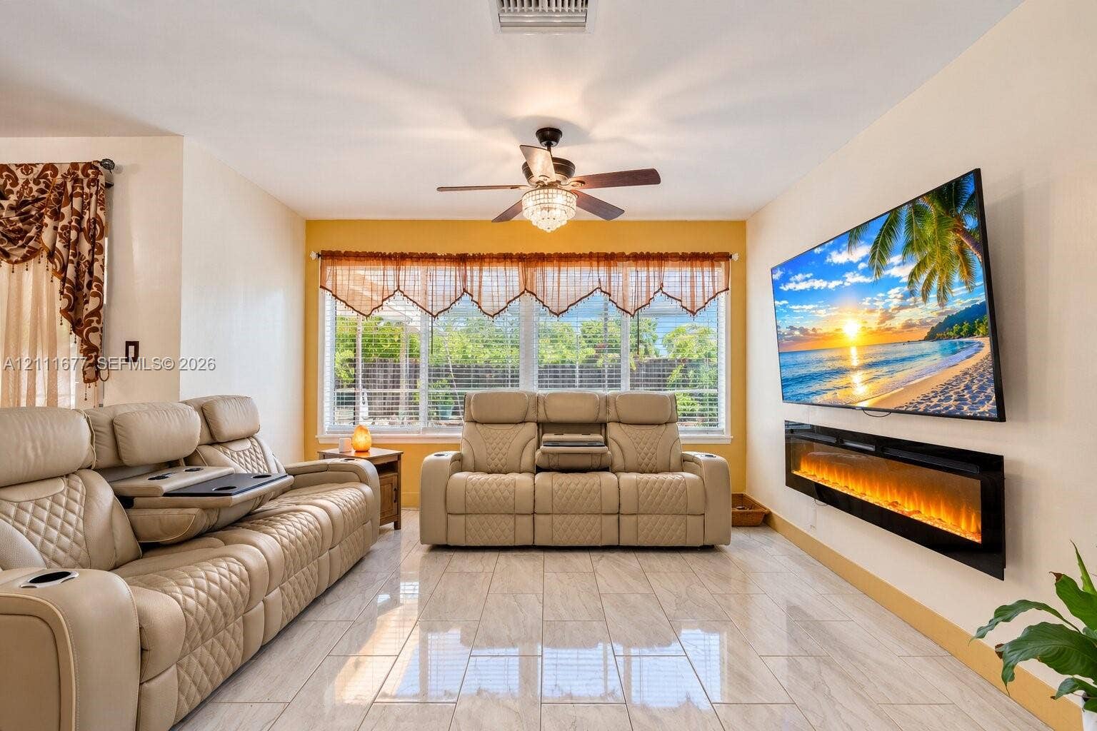 1921 Acapulco Drive, Miramar, FL 33023 Living area featuring polished tile flooring, wall-mounted electric fireplace, ceiling fan with integrated lighting, and multiple windows