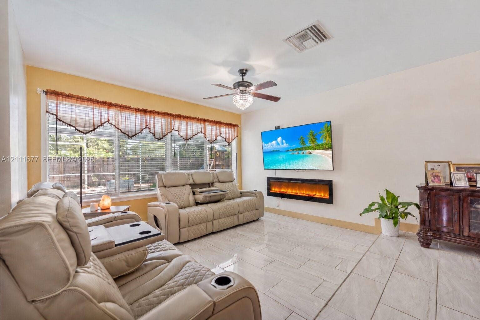 1921 Acapulco Drive, Miramar, FL 33023 Living area featuring large format tile flooring, a wall-mounted electric fireplace, and a ceiling fan with integrated lighting