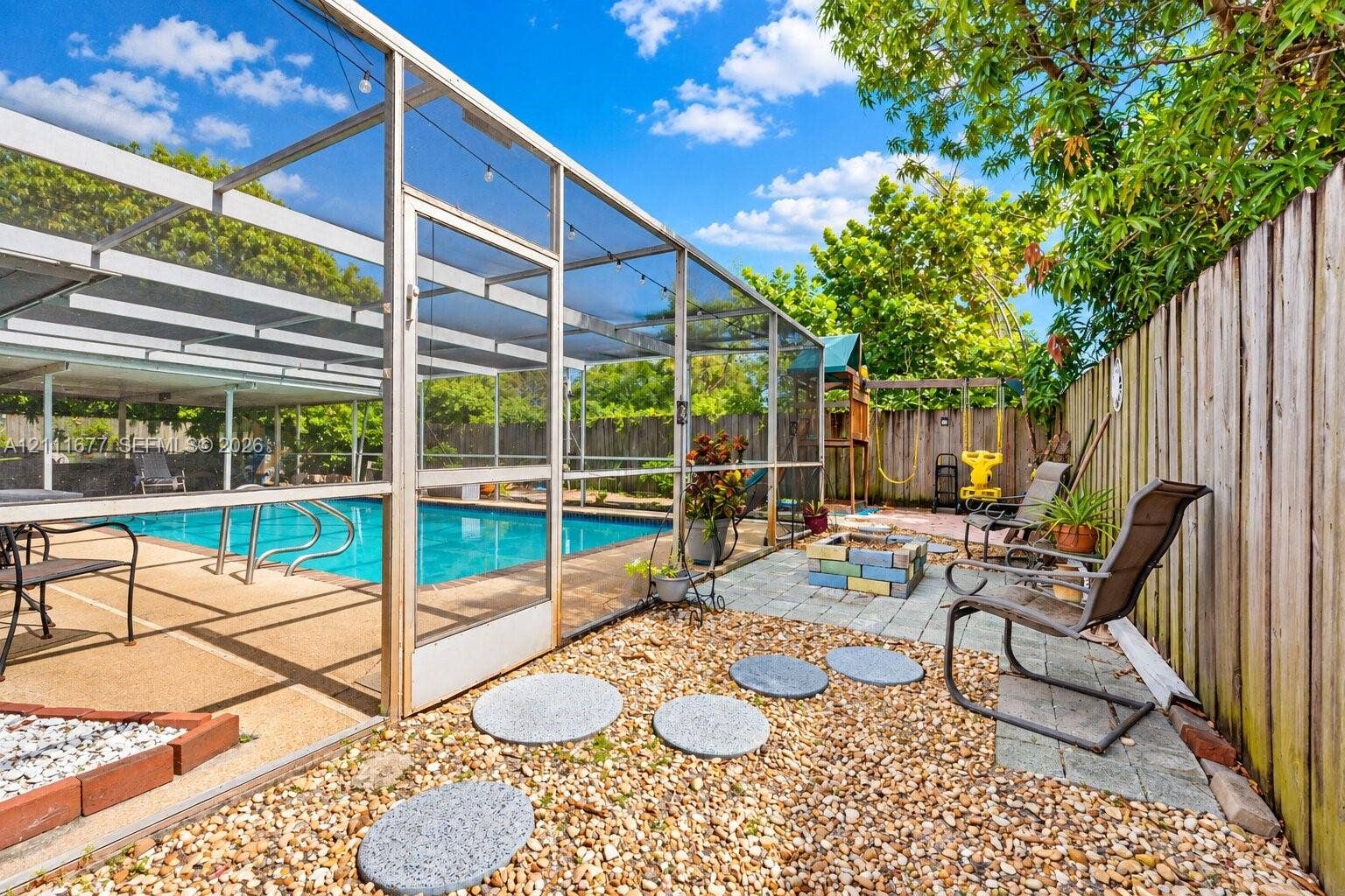 1921 Acapulco Drive, Miramar, FL 33023 Screen-enclosed swimming pool featuring a concrete deck and a stone paver patio area with a built-in fire pit