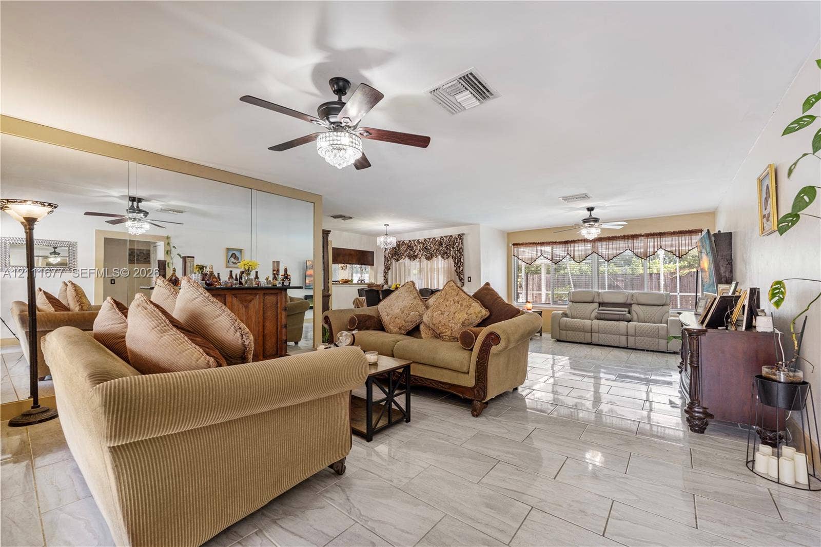 1921 Acapulco Drive, Miramar, FL 33023 Spacious living area featuring polished tile flooring, wall-to-wall mirrored accent, and two ceiling fans with integrated lighting fixtures