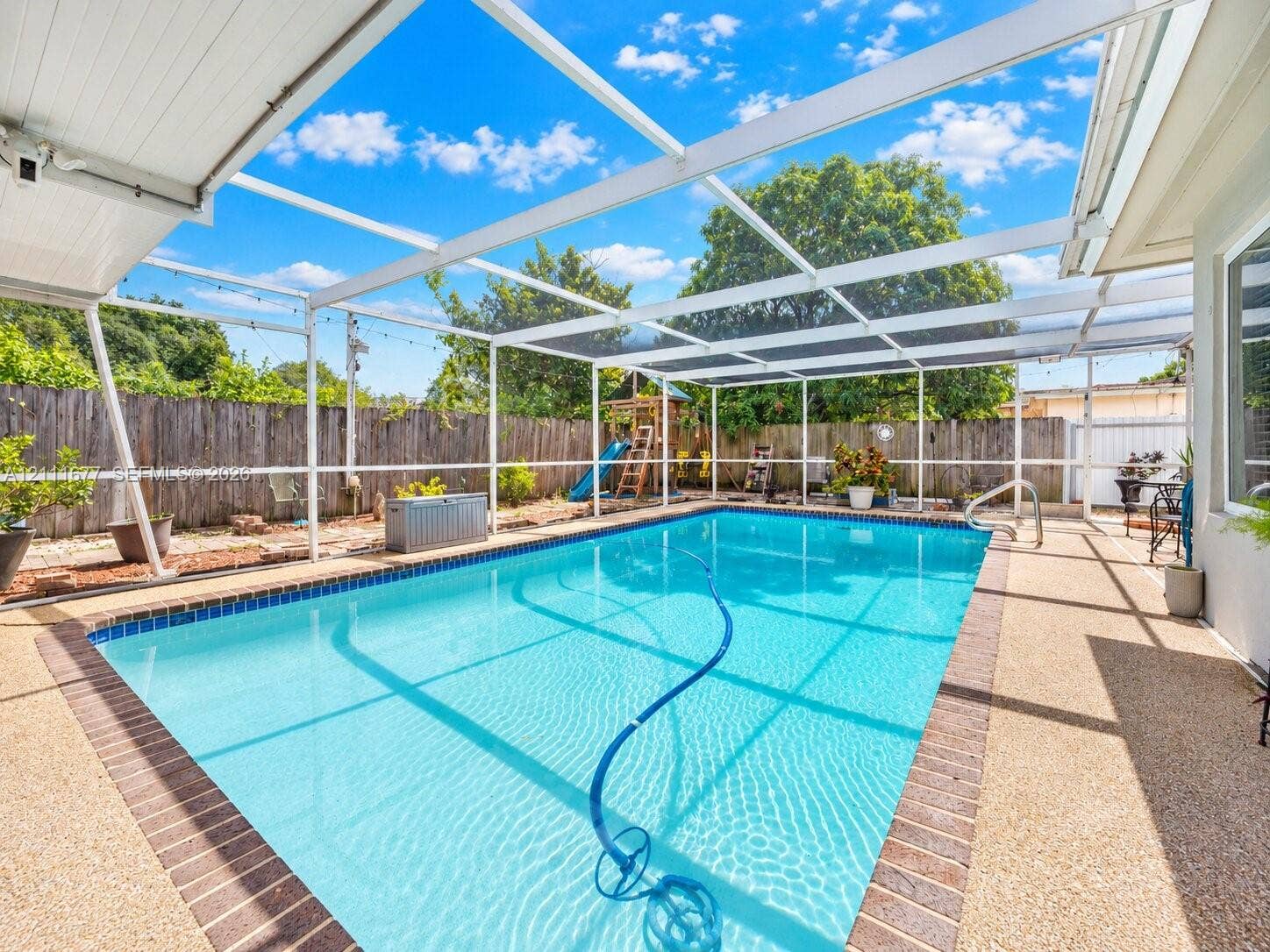 1921 Acapulco Drive, Miramar, FL 33023 In-ground swimming pool with brick paver coping and screened-in enclosure, featuring an exposed aggregate pool deck and perimeter wood privacy fencing