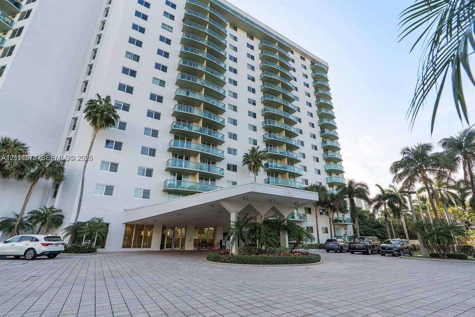 High-rise exterior featuring a tiered faade with private glass-railed balconies, a covered porte-cochre entry, and a paved arrival plaza with circular landscaping